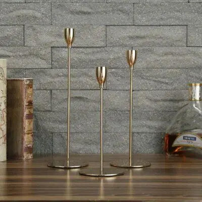 Three gold candle holders on a wooden surface with a stone wall background