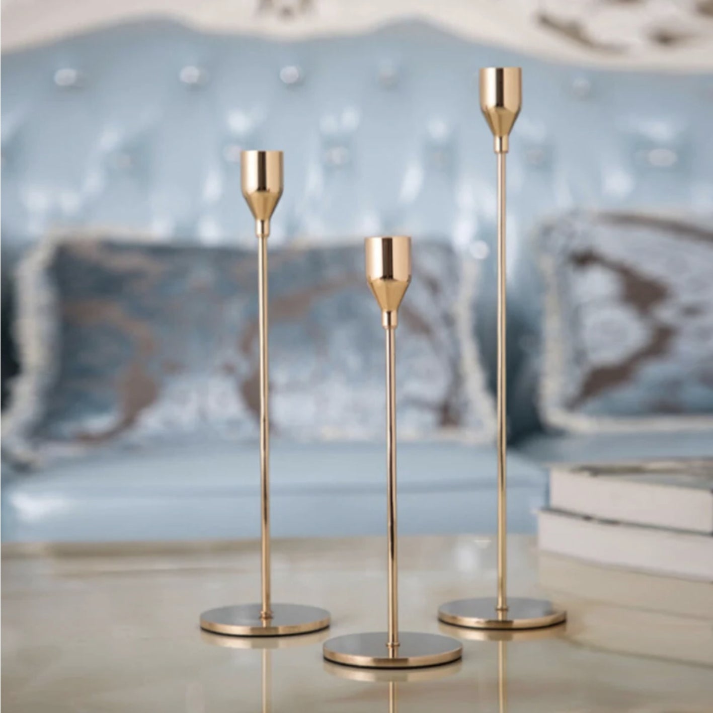 Three gold candle holders on a reflective surface with a blurred decorative background