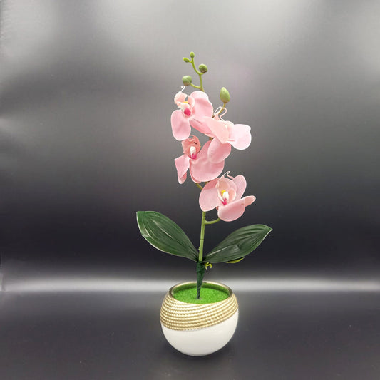 Artificial pink orchid plant in a white pot with gold stripes on a dark background