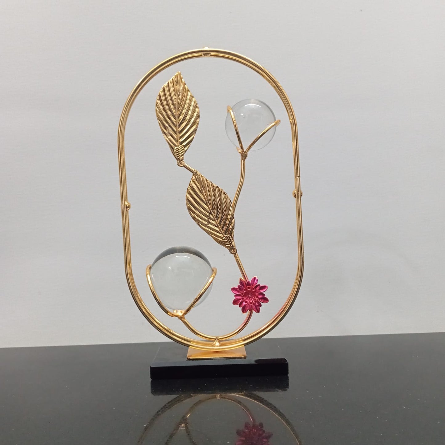 Decorative piece with gold leaves and a pink flower on a black base against a gray background