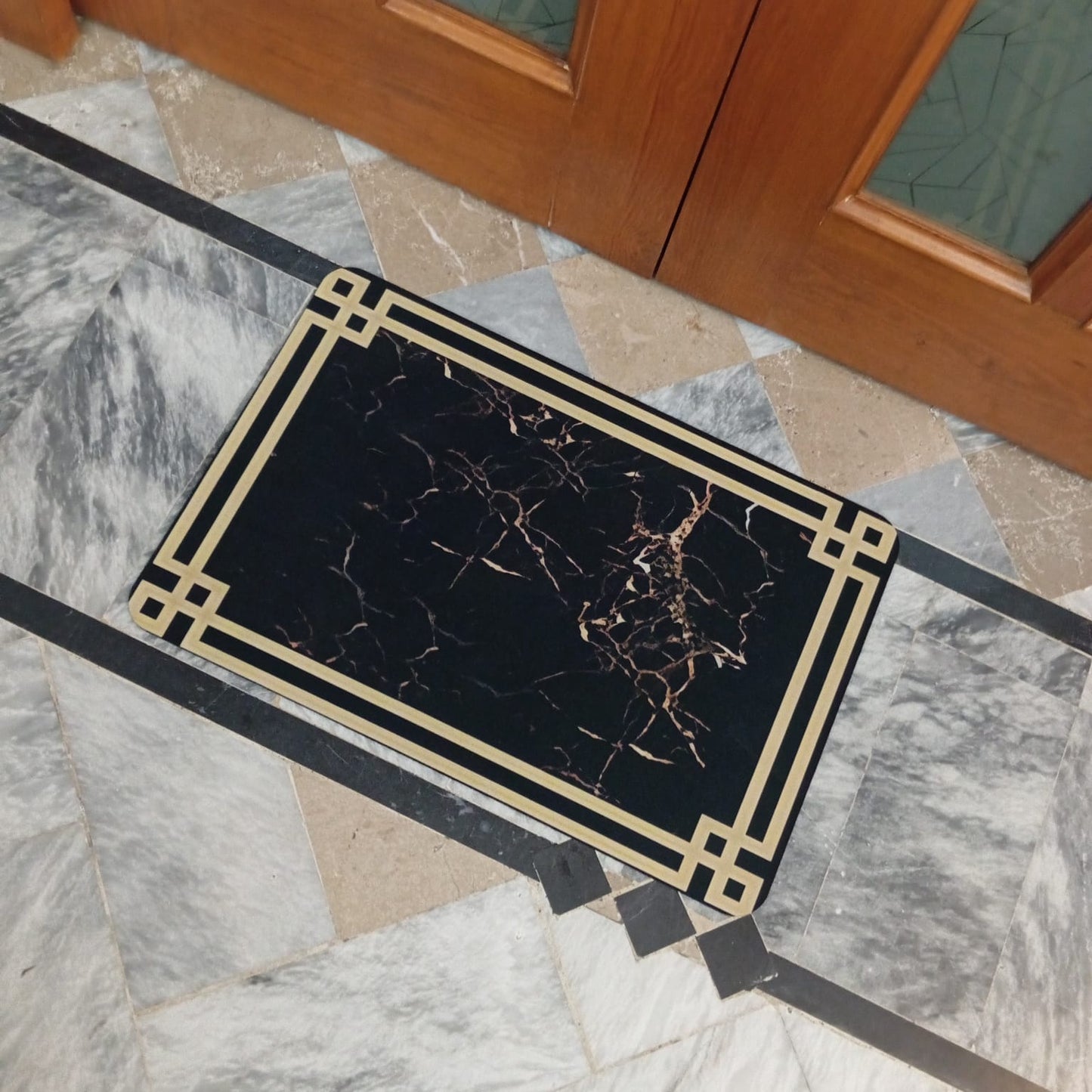 Decorative doormat with black and gold design on a marble floor.