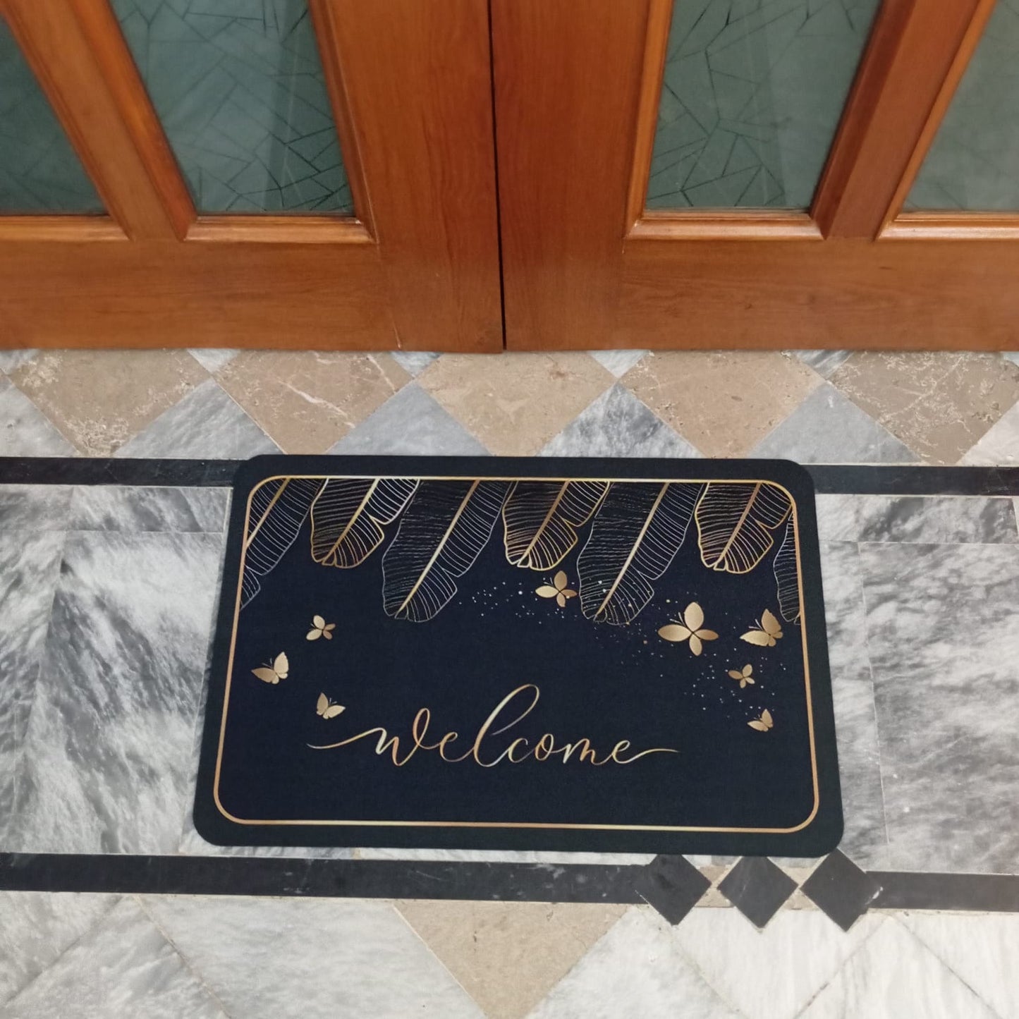Decorative doormat with floral and butterfly design on a marble floor in front of a wooden door.