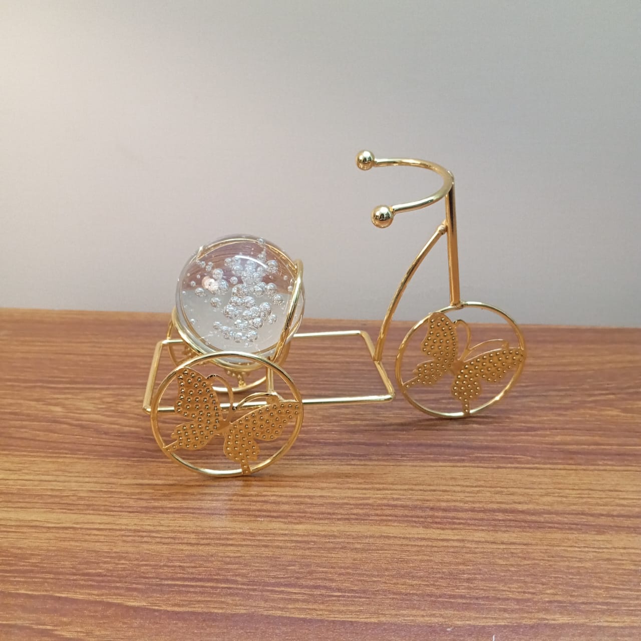 Gold decorative tricycle with a clear crystal ball on a wooden surface