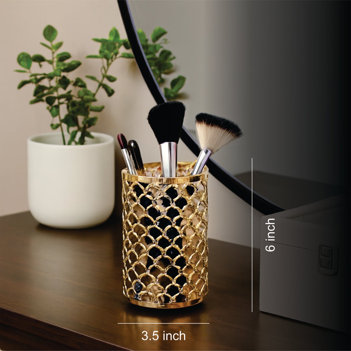 Gold decorative pen holder with makeup brushes on a desk next to a plant