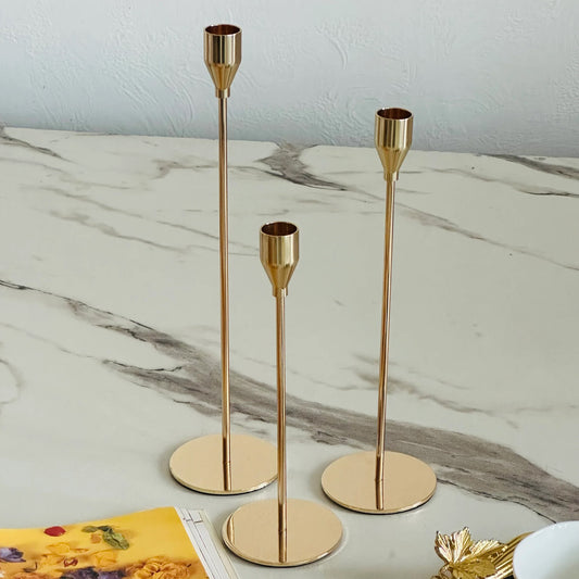 Three gold candle holders on a marble surface with a light blue wall in the background.