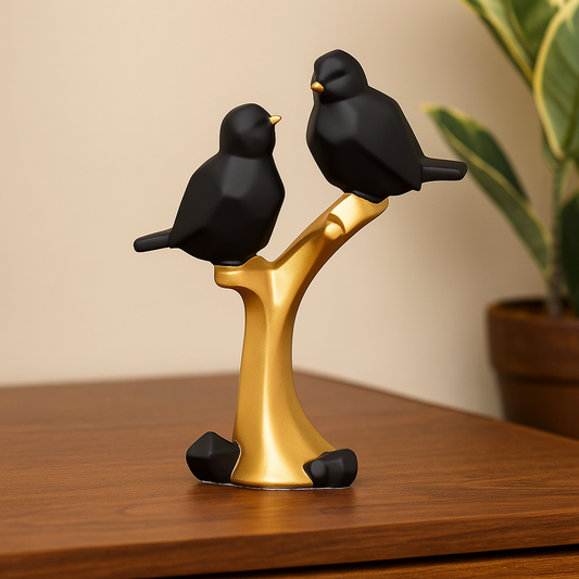 Decorative sculpture of two black birds on a gold branch on a wooden surface.