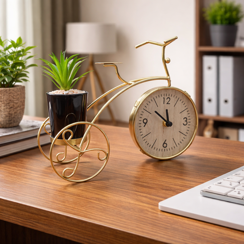 Decorative clock shaped like a bicycle on a desk with plants and a lamp in the background