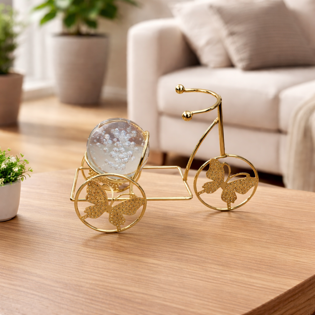 Decorative gold bicycle with a glass sphere on a wooden table in a living room setting.