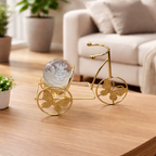 Decorative gold bicycle with a glass sphere on a wooden table in a living room setting.