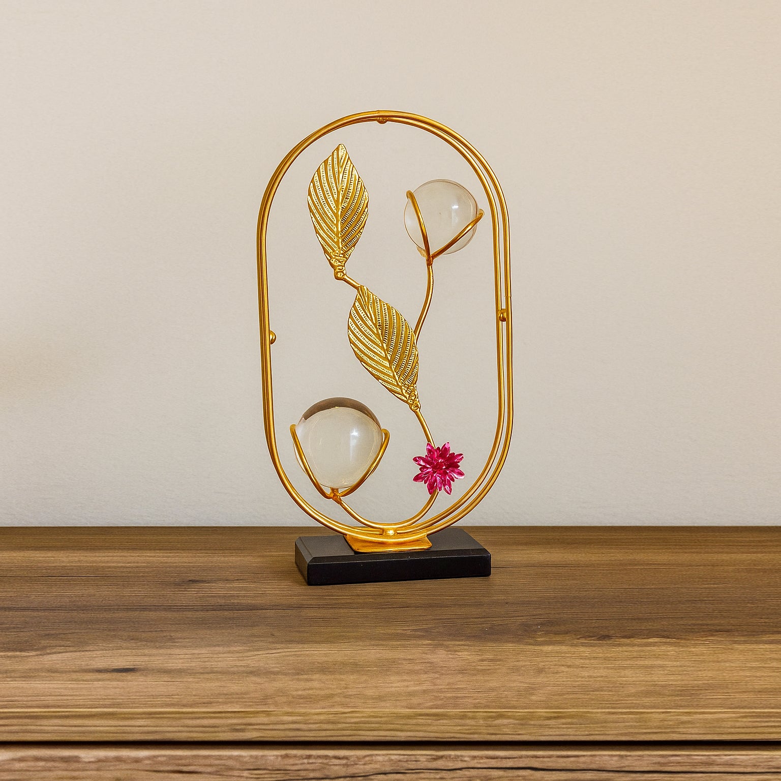 Decorative lamp with gold frame, leaves, and a pink flower on a wooden surface.