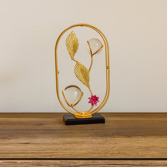 Decorative lamp with gold frame, leaves, and a pink flower on a wooden surface.