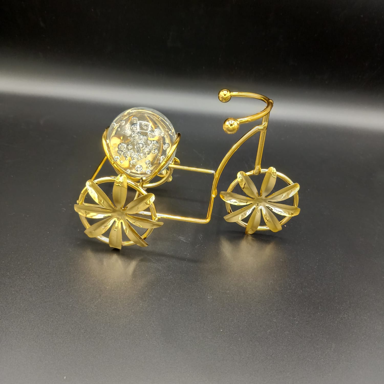 Gold bicycle-shaped jewelry piece with a clear gemstone on a dark background