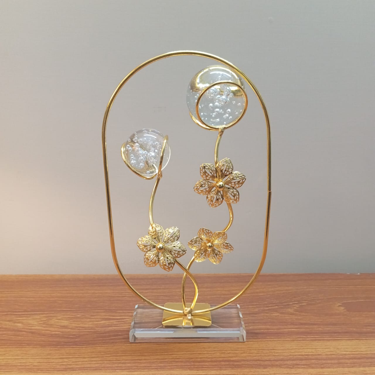 Decorative gold floral sculpture on a clear base against a neutral background