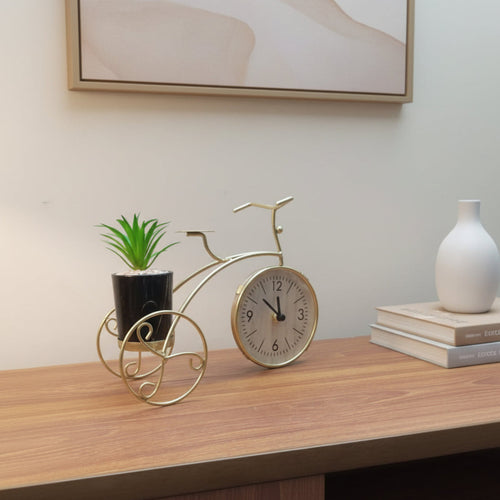 Decorative clock shaped like a bicycle with a plant on a wooden surface