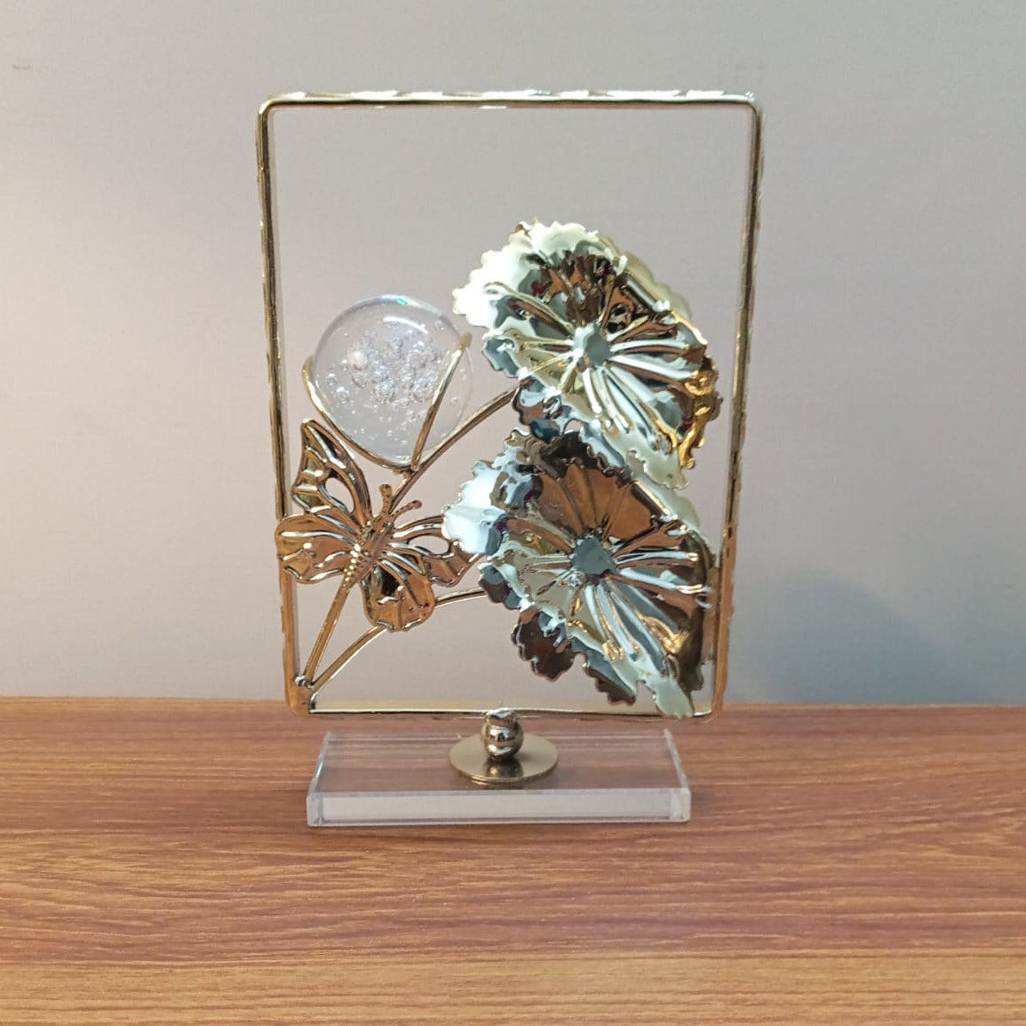 Decorative piece with butterflies and a crystal ball on a stand against a plain background