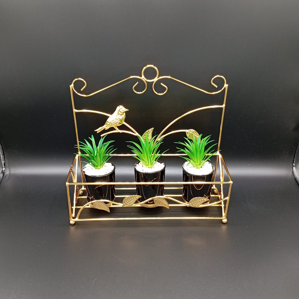 Decorative gold metal stand with three small potted plants on a black background