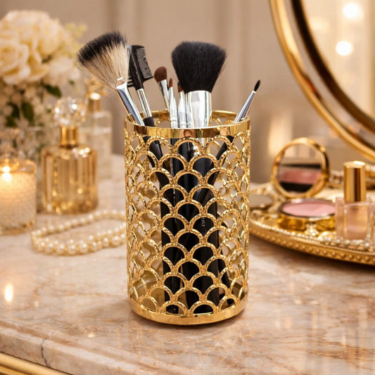 Gold decorative holder with makeup brushes on a vanity table with mirror and candles.