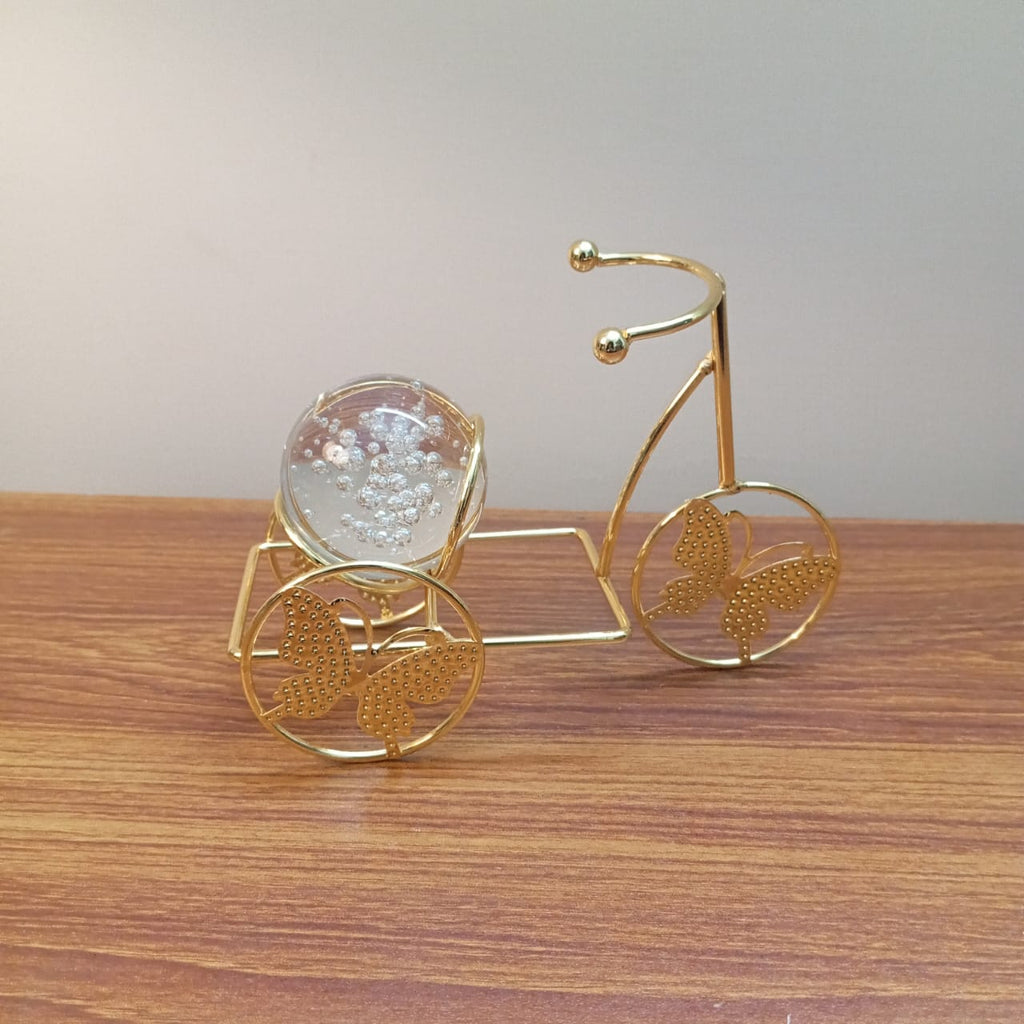 Gold decorative tricycle with a clear crystal ball on a wooden surface
