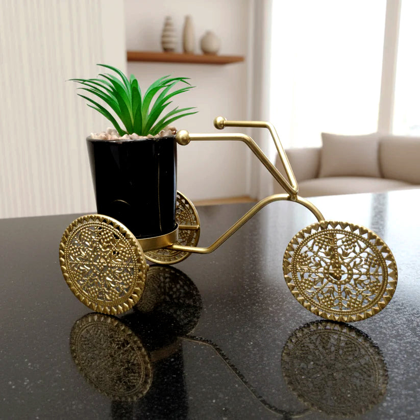Decorative gold bike planter with a plant on a reflective surface
