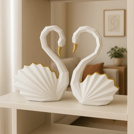 Two white swan sculptures with gold accents on a shelf in a home setting.
