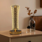 Decorative table lamp with a glass shade on a surface next to a bottle and a plant.