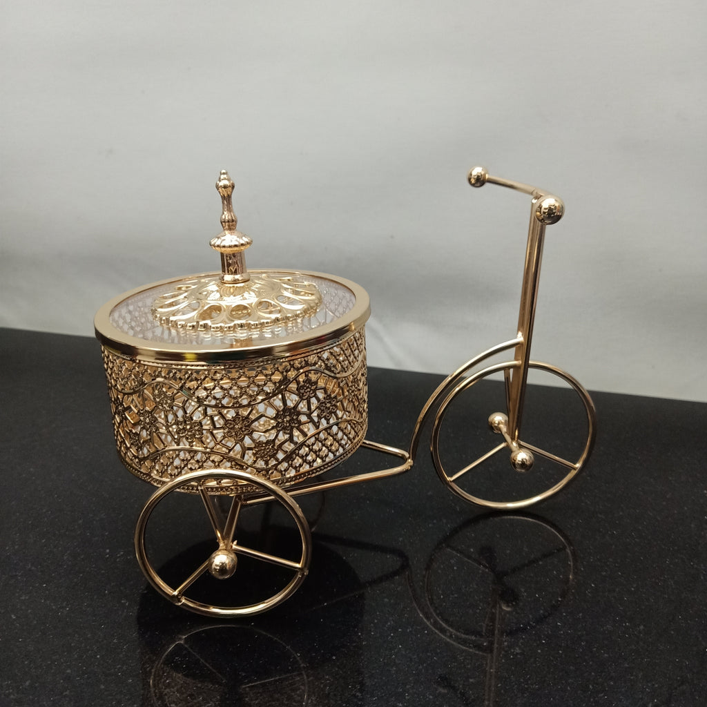 Decorative gold bicycle with a round container on a black surface