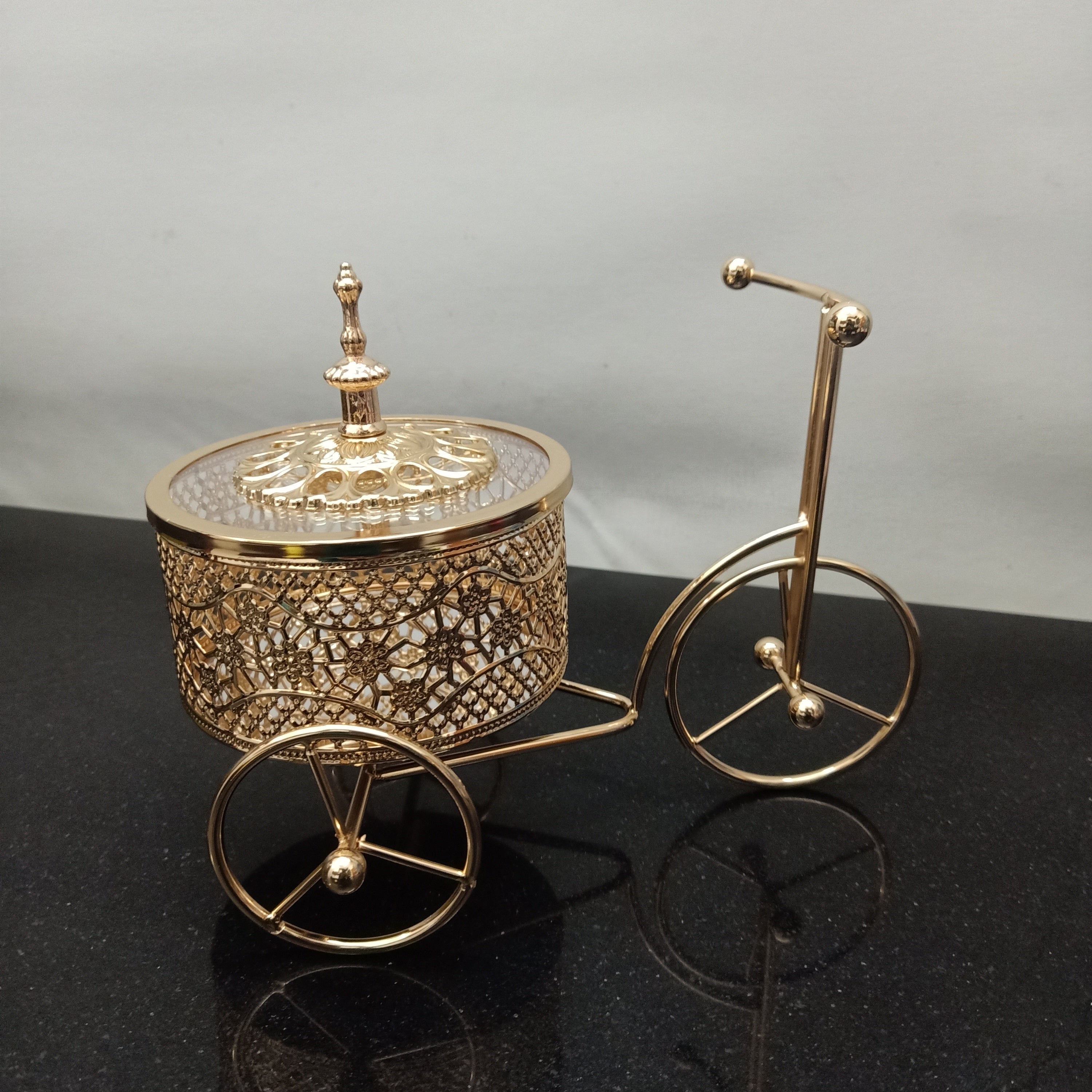 Decorative gold bicycle with a round container on a black surface