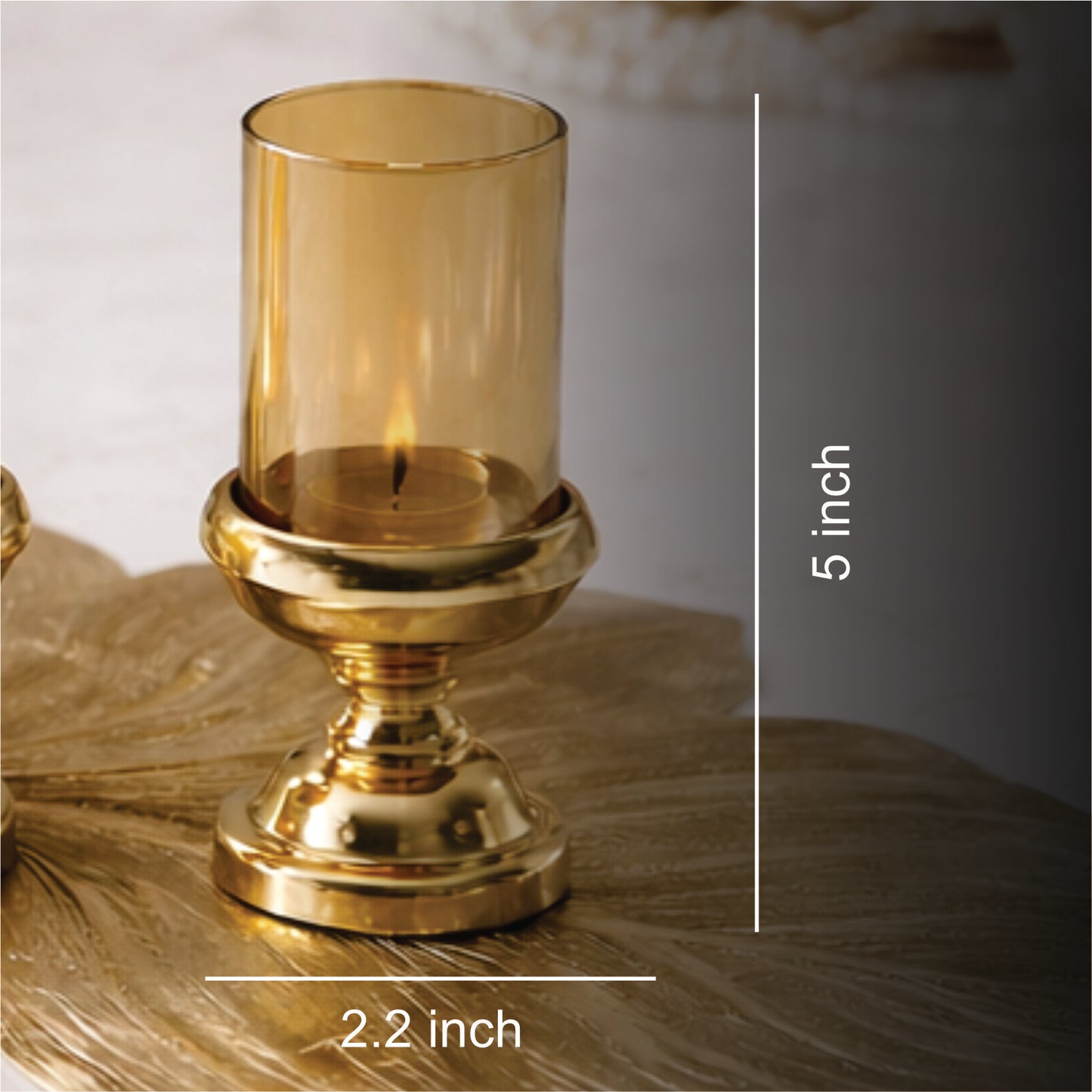 Gold candle holder with amber glass on a textured surface, with measurements indicated.